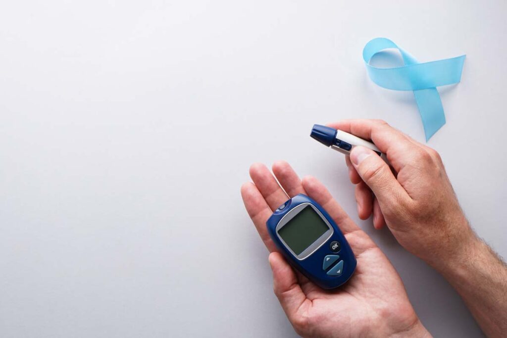 Digital blood glucose meter, lancet pen in male hands on a gray background with a blue ribbon, flat lay. Space for text. World Diabetes Day, November 14th.